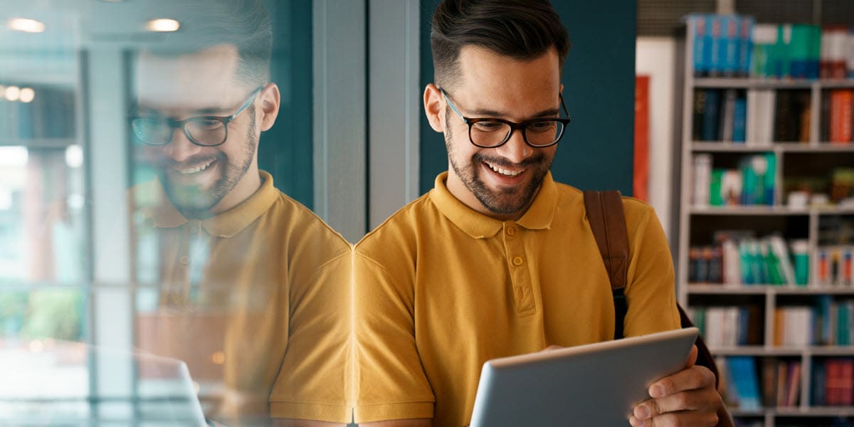 Man smiling at tablet with bookcase in background