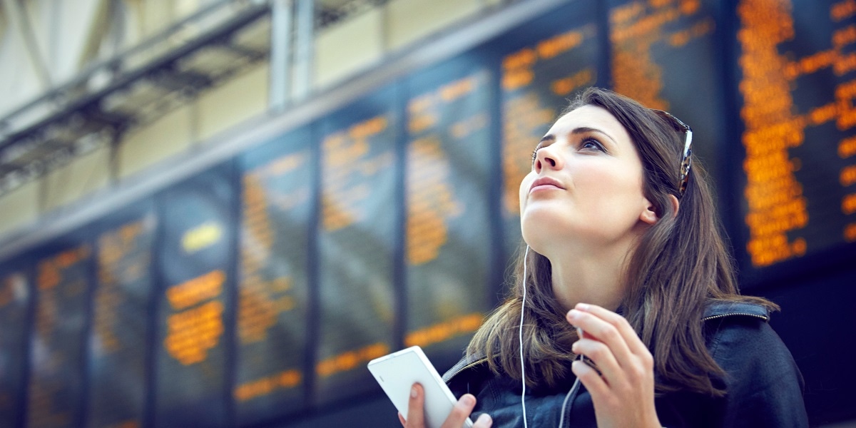 Woman in an airport with headphones in and a phone in her hand